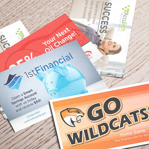A collection of printed promotional materials scattered on a table. Visible items include a "Go Wildcats!" home game flyer, a 1st Financial advertisement featuring a piggy bank, and various other cards promoting services like oil changes and financial success tips.