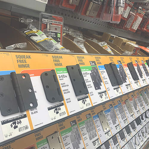 A store display shelf shows various types of door hinges in different sizes and features, such as "squeak-free" and "matte black." The hinges are individually packaged and labeled with prices ranging from $3.88.