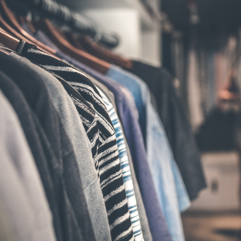 A close-up shot of various shirts hanging on wooden hangers in a clothing store. Different colors and patterns of shirts are neatly organized on a metal rack, creating the kind of visually pleasing array you'd find in bustling markets.
