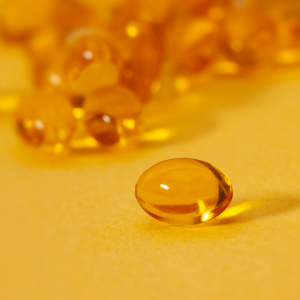 Close-up of a translucent amber-colored gel capsule against a matching yellow background. In the background, several other capsules are blurred, creating a sense of depth and focus on the single foreground capsule. This image captures the precision found in health supplement markets.
