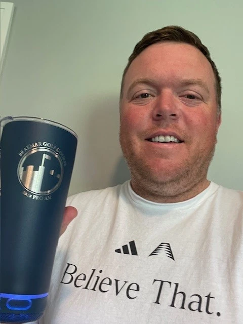 A person holds a blue tumbler with a golf event logo, wearing a white Adidas shirt that reads "Believe That." The tumbler, dated August 20th, 2024, showcases promotional products with the "3.2 PRO AM" design.