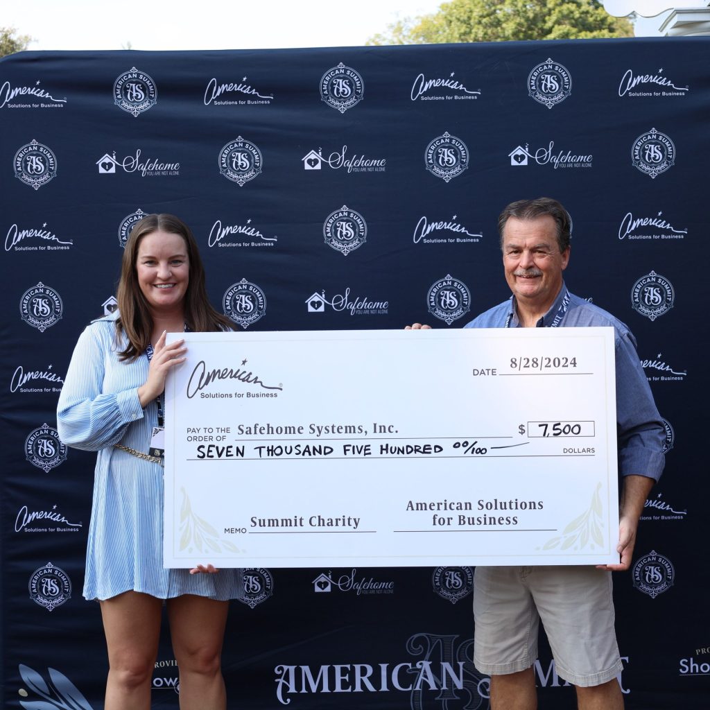 A woman and a man proudly hold a large check for $7,500 from ASB, made out to Safehome Systems, Inc. They stand before a branded backdrop adorned with Summit Charity logos and text, celebrating the success of the fundraising event.