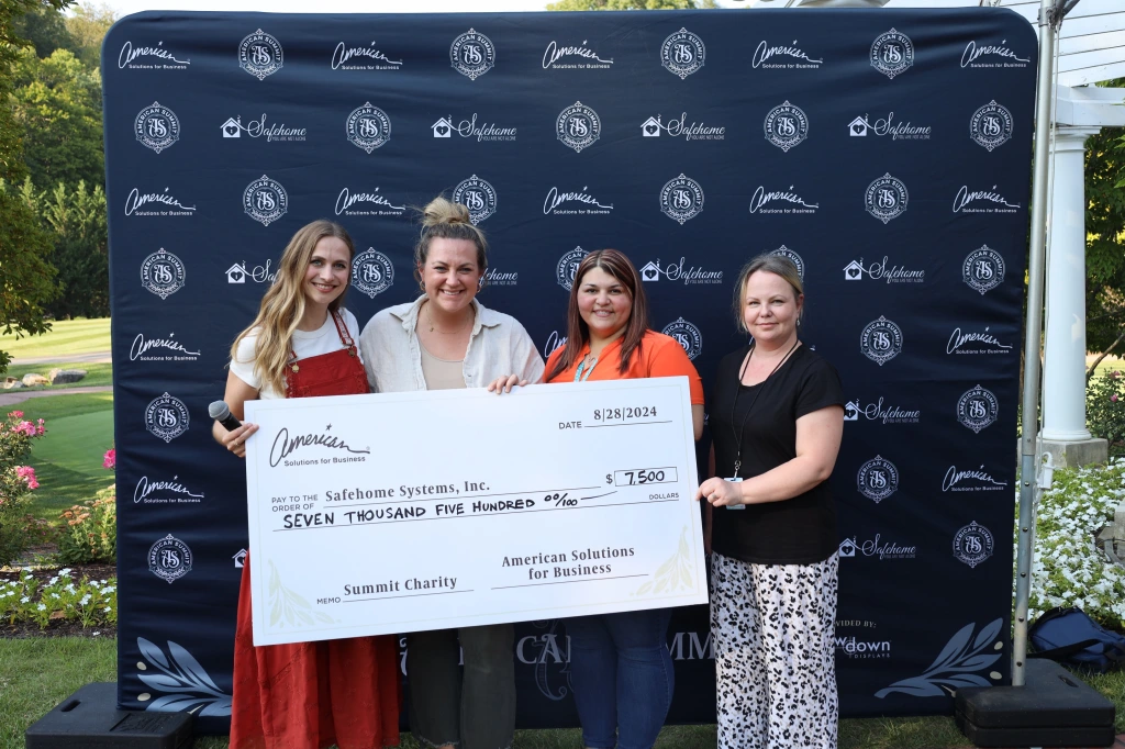 Four people stand outdoors before a "Candleridge Dawn" backdrop, smiling as they hold a large ceremonial check for $7,500 made out to Safehome Systems, Inc. This fundraising event showcases their commitment to supporting community safety initiatives.