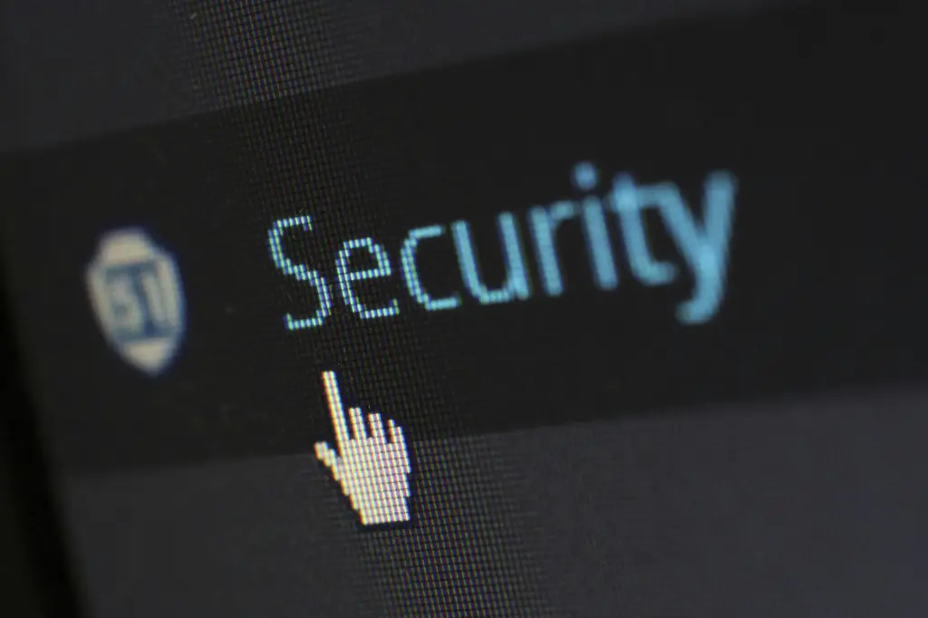 A computer screen displays the word "Security" next to a shield icon, with a hand-shaped cursor pointing at it. The image underscores cybersecurity's role in ensuring business continuity for dealerships and other businesses.