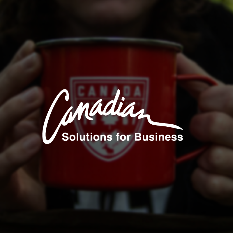 A person holds a red mug with a Canada logo and the text "Solutions for Business" on it. The mug has a white maple leaf emblem. The image is slightly blurred, focusing on the text.