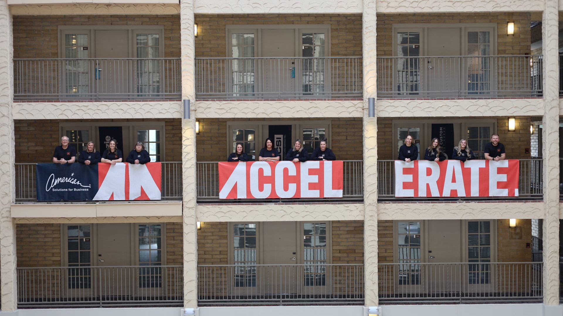 People stand on three stories of a building’s interior balconies, behind large red and white banners reading “ACCELERATE” at the ASB Accelerate Event in Bloomington MN. One banner on the left says "American Association of Anatomists.