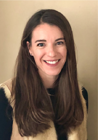 A woman with long brown hair and a light complexion is smiling at the camera, celebrating her role as one of the ASB Advisory Board Members. She wears a black top and beige vest, standing before a plain, light-colored background.