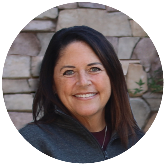 Becky Thesing, Vendor Relations Manager at American Solutions for Business, smiles warmly in front of a light-colored stone wall, her long dark hair cascading over a dark jacket.