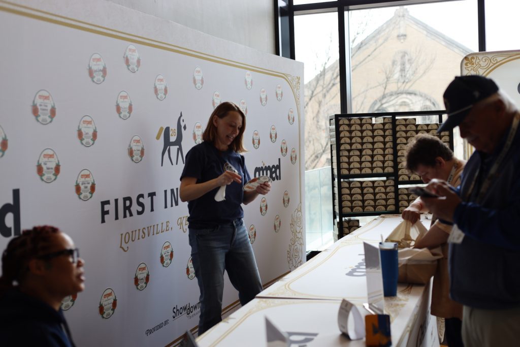 A woman stands behind a sign-in table at the National Sales Conference, smiling and holding papers. Two people in front are signing in, while another sits at the end. An ASB-branded backdrop and boxes are visible in the Louisville, Kentucky venue.