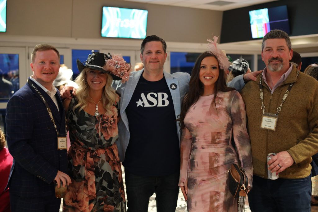Five people pose together at the National Sales Conference in Louisville, Kentucky. Two women in floral dresses and hats join three men in jackets—one center man sports an "ASB" T-shirt. All are smiling and enjoying themselves.