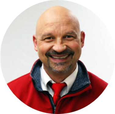 Nate Disrud, Senior Director of Technology at American Solutions for Business, is a smiling bald man with a mustache and goatee, wearing a red jacket, white shirt, and red tie against a plain white background.