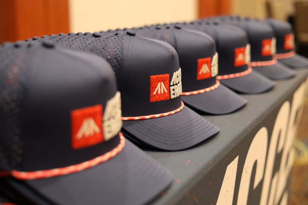 A row of navy blue trucker hats with red and white patches and braided bills is neatly lined up on a table at the 2026 ASB Accelerate Event in Duluth, MN.